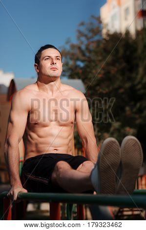 Young muscular build man doing pull ups exercises on horizontal bar outdoors, strong athletic man with naked torso training hard at sunny afternoon outside, sportsman working out. Healthy lifestyle.