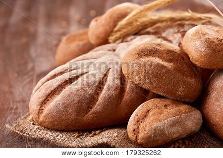 handmade tasty bread lying on burlap on the wooden table with flour, wheat and ears of wheat. Brown bread and rulls. Delicious food. Fresh baking. Tasty and appetizing.