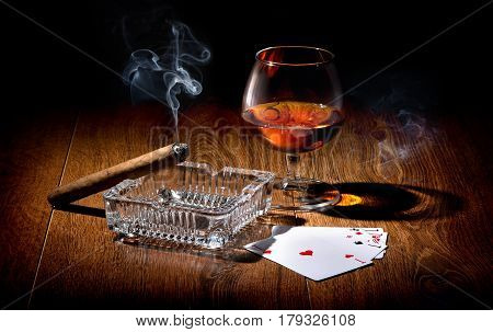 Playing cards near wineglass of whiskey and cigar
