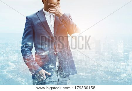 Close up of an unrecognizable businessman in a suit rubbing his chin while satanding against a city panorama. Double exposure