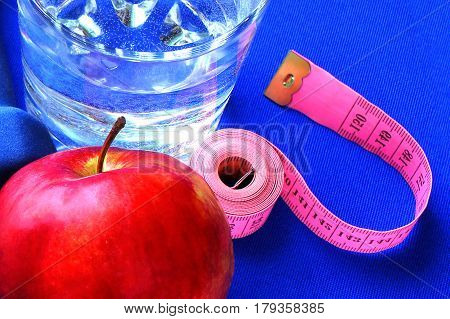 Close up of a pristine red apple two dumbbells  and glass water, blue atheletic small rug of   with reflection , sound lifestyle