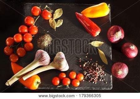 Top view of a dark board and vegetables with spices for cooking copyspace.