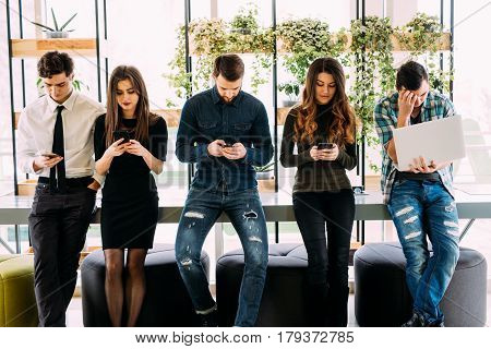 Group Of Friends Standing On Table And Browsing In Their Divices In Modern Room