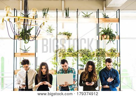Group Of Friends Standing On Table And Everyone Use His Divices In Modern Office Room. Together Fun