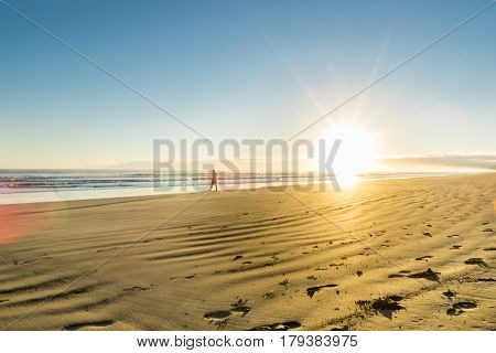 Golden beach huer at sunrise over wide flat sandy beach at Ohope Whakatane New Zealand with distant silhouette of man walking