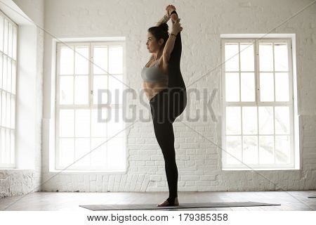 Young yogi woman practicing yoga concept, Variation of Utthita Hasta Padangushthasana pose, Trivikramasana, standing splits, working out, wearing sportswear, full length, white loft studio background