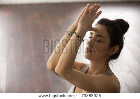 Young beautiful sporty yogi woman practicing yoga concept, doing namaste gesture, her eyes closed, namaste hands to forehead, working out, meditating, breathing, studio background