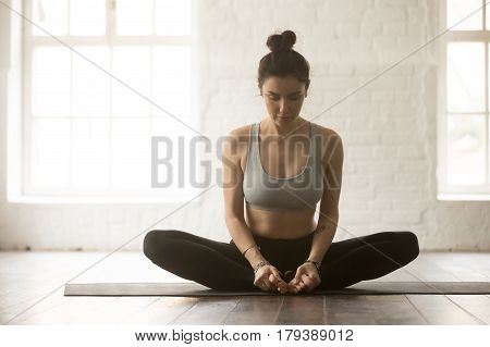 Young attractive yogi woman practicing yoga concept, sitting in baddha konasana exercise, Butterfly pose, working out, wearing sportswear bra and pants, full length, white loft studio background