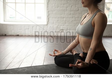 Young cool attractive yogi woman practicing yoga concept, sitting in Padmasana exercise, Lotus pose, working out, wearing sportswear bra and pants, midsection close up, white loft studio background