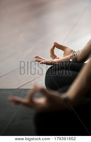 Close up of mudra gesture, performed with female fingers, yogi woman meditating in lotus pose, wearing wrist bracelet, sitting in Padmasana exercise, vertical photo. Meditation session concept