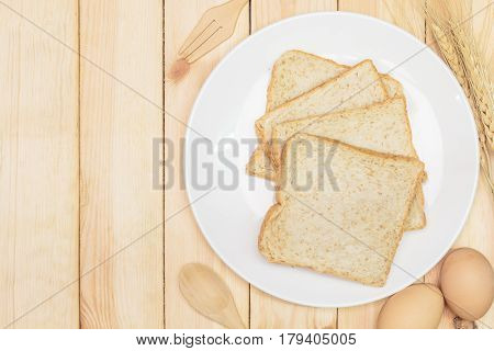 Sliced wholemeal bread on white plate with wheat ears and egg on wooden table background Top view with copy space and text.
