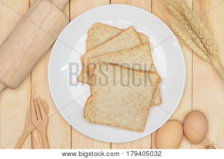Sliced wholemeal bread on white plate with wheat ears and egg on wooden table background Top view
