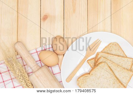 Sliced wholemeal bread on white plate with wheat ears and egg on wooden table background Top view with copy space and text.