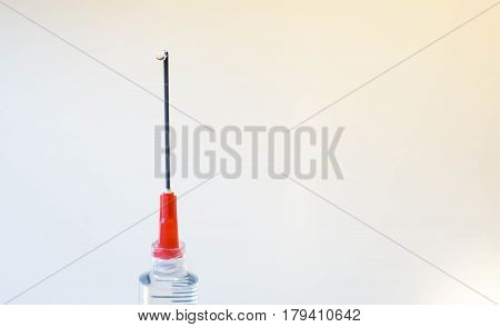 A syringe needle is help vertically and a drip of fluid exits and runs down the needle against a white background
