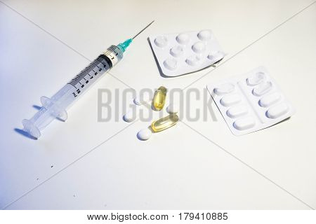 A variety of medication including a syringe with a green tip two blister packs white pills and yellow plastic pills full of cod liver oil vitamin D supplement against a white background