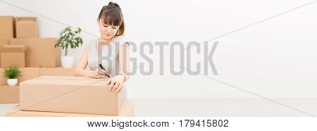 Young woman signs a box while moving. Cleaning and packing. The concept of move.