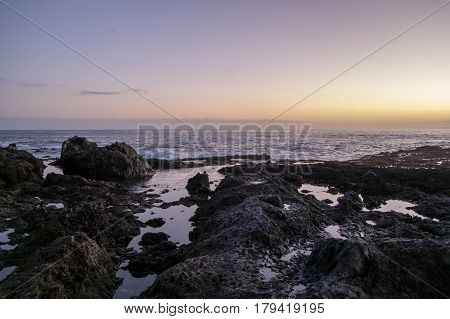 Sun setting over the black volcanic rocks and rock pools on the Tenerife coast with the waves of the Atlantic Ocean