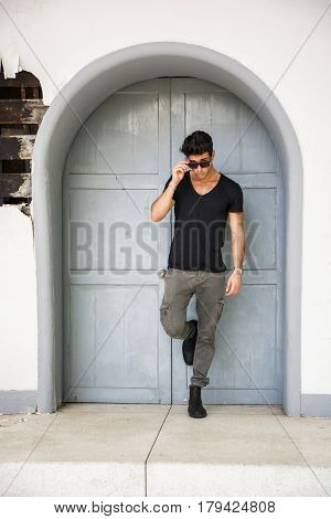 Handsome young man outdoors in front of old house's wood entrance door, looking away to a side