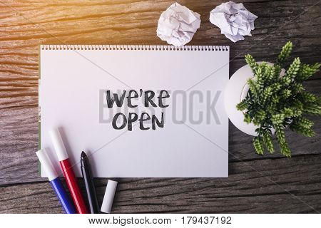 We're Open Word With Notepad And Green Plant On Wooden Background.