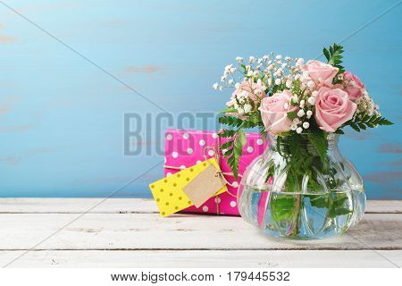 Rose flower bouquet in glass vase and gift box over wooden background