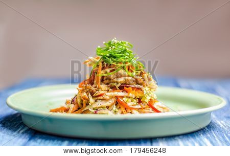 Salad of meat and vegetables with sesame and green algae on a green plate on a blue denim background