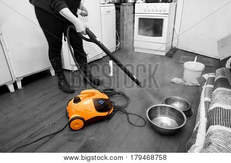 Woman cleaning floor with steam or hot water spray kitchen interior. Selective color shot
