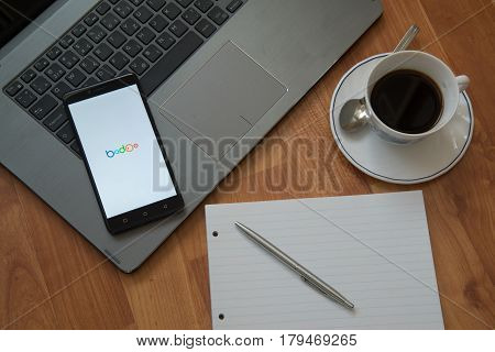 Nitra, Slovakia, march 28, 2017: Badoo application in a mobile phone screen. Workplace with a laptop, an earphones, notepad, pen and coffee on wooden background