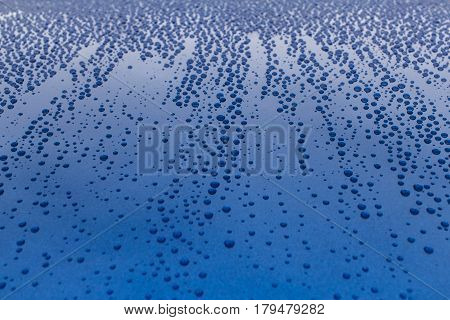 Many drops of water on a blue surface. Traces of rain on the hood of the car.