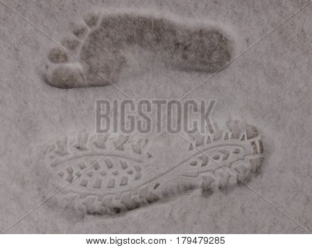 Imprint of a shoe next to a bare foot print on the snow. Right foot without shoe. Left foot in shoe.