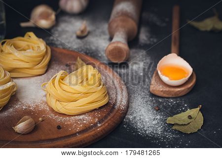 Raw homemade pasta and ingredients for cooking on a black background. Uncooked noodles with flour egg and spices. Food and culinary concept.