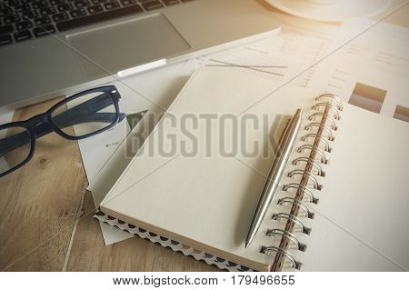 office desk mockup: laptop computer notebook pen and cup of coffee with business financial graph on wooden table.. Vintage filter effect.