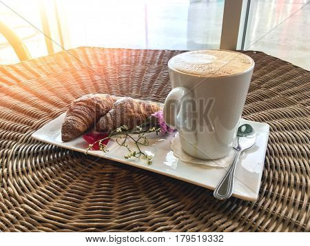 hot cappuccino coffee drink with croissants decorate with flower on rattan wood table