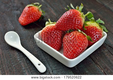 Strawberry fruit on wood background. Forest fruit in white idaeus and spoon. Delicious fresh berries.