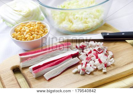 Surimi sticks cut on wooden cutting board. Process of cooking Chinese cabbage sweet corn and surimi salad.
