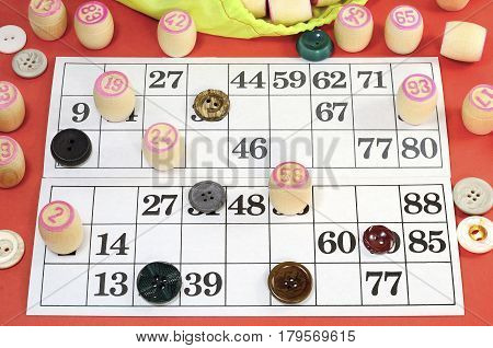 photograph of details of Russian vintage game Bingo or Lotto with white paper cards in the cells which contain numbers small wooden barrel on which is written the numbers green bag multi-colored buttons on the table red color
