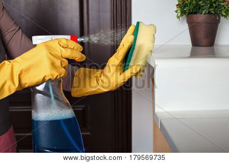 Female hands in gloves cleans the shelf with spray