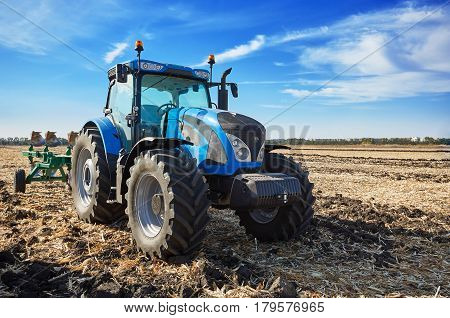 Tractor working in a field, agricultural machinery in the work, machine cultivates the land, tractor in the background cloudy sky