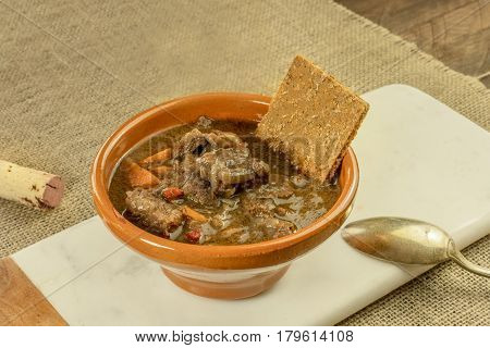 Meat and vegetable stew in an earthenware bowl, with a flatbread and a wine cork