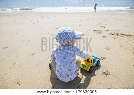 Baby boy playing on the sand while his sister run beside beach shore. El Rompido Cartaya Huelva Spain