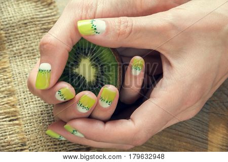 Kiwi and skin care of a beauty female hands with green and white moon nail art manicure on a sackcloth and wooden background
