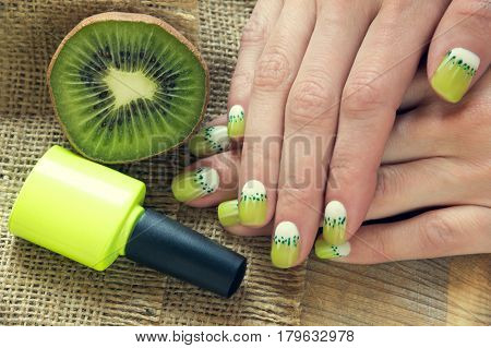 Kiwi, nail polish and skin care of a beauty female hands with green and white moon nail art manicure on a sackcloth and wooden background