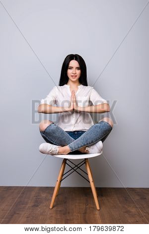 Beautiful Young Woman Sitting On Chair In Lotus Pose Against Gray Background