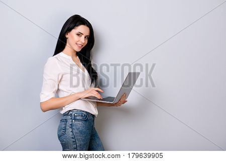 Happy Young Woman In Casual Clothes Using Laptop And Checkin While Standing On Gray Background