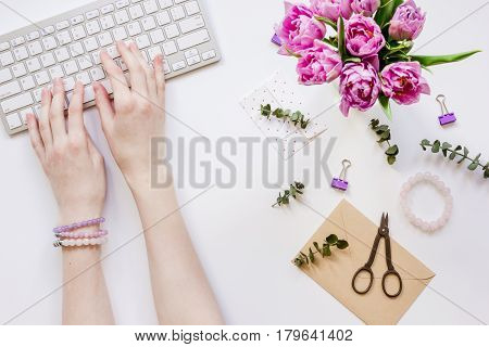 Spring pink flowers and hands on workdesk at home ofiice white background top view