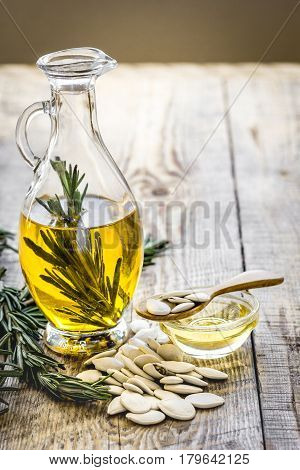 extra oil in carafe with pepitas and fresh rosemary on wooden desk background