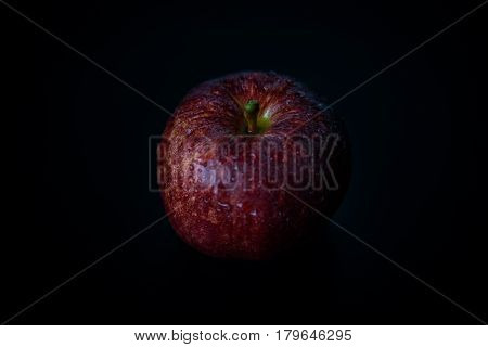 Low key close up of red apple against black background.