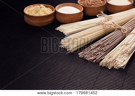Raw japanese noodles with ingredient in wooden bowls on black striped mat background with copy space.