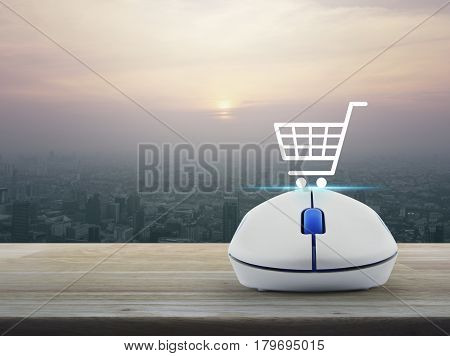 Shopping basket icon with wireless computer mouse on wooden table over modern city tower at sunset vintage style Shop online concept