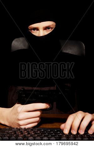 Dangerous hacker in balaclava holding gun