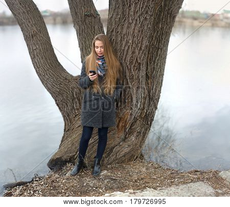 Portrait Of A Beautiful Girl With A Phone In Early Spring Outdoors.